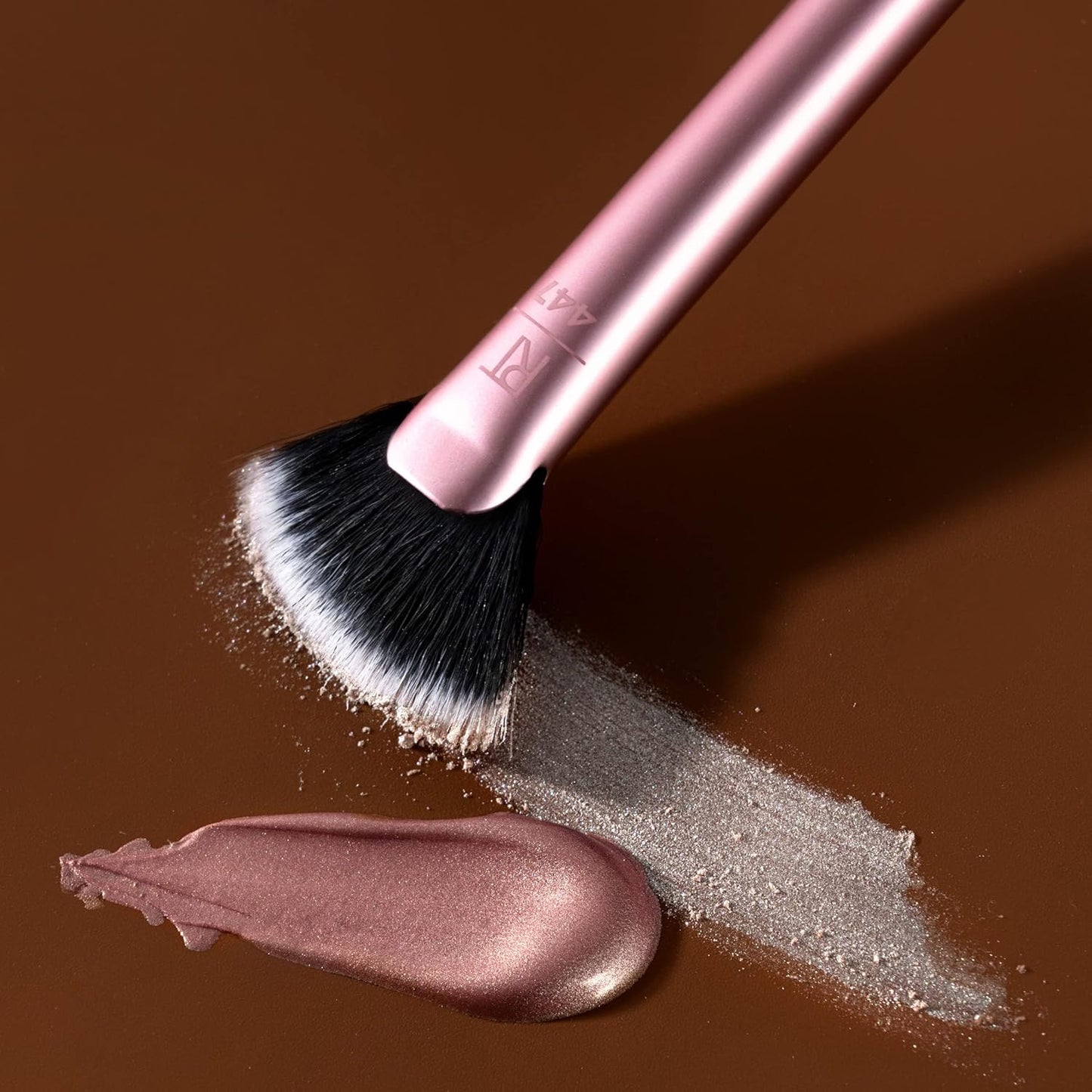 Makeup brush with pink handle on a brown background with makeup product