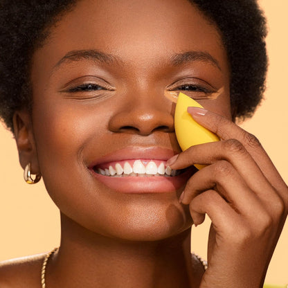 Woman applying a yellow cosmetic product to her face against a beige background