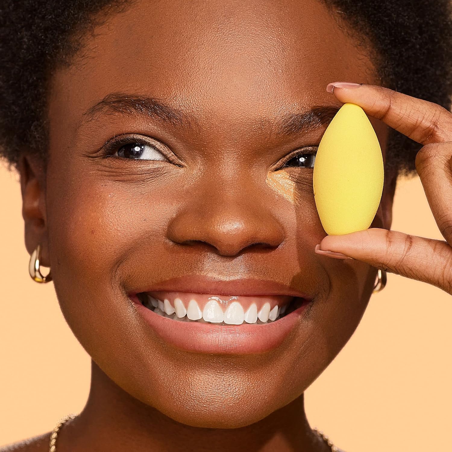 Woman applying makeup with a yellow sponge applicator on a beige background