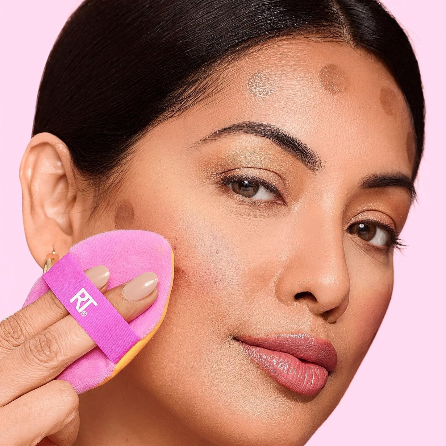 Woman applying makeup with a pink brush on a pink background