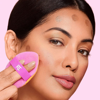 Woman applying makeup with a pink brush on a pink background