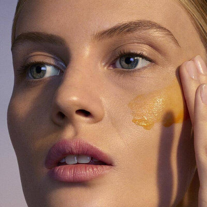 Model applying orange skincare product to her face for rejuvenated and radiant skin.