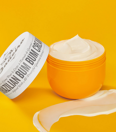 Orange jar of  Sol de Janeiro 'Bum Bum Bum' cream with open lid on a yellow background
