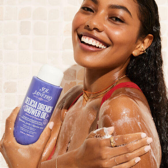 Woman enjoying Sol de Janeiro Delicia Drench Shower Oil while showering, showcasing radiant and hydrated skin.