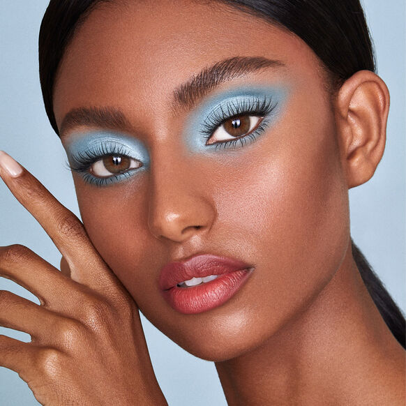 Close-up of a model with SWEED blue eyeshadow and pink lipstick against a light blue background