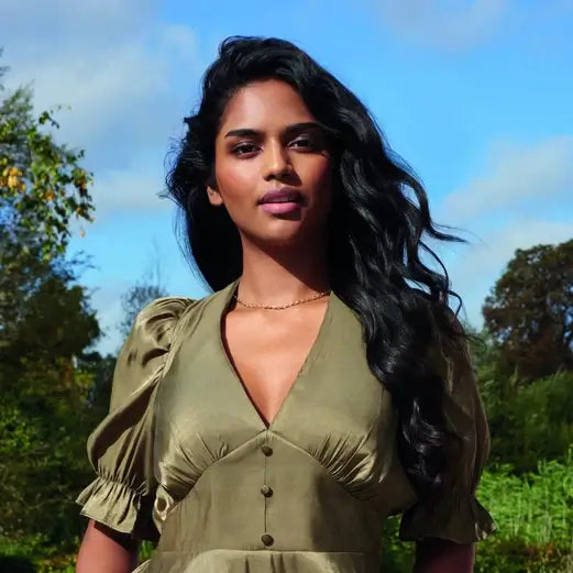 Woman with long wavy hair wearing an olive green dress in a natural outdoor setting.