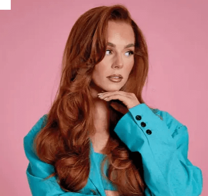 Model showcasing long, wavy red hair and turquoise blazer against a pink background.