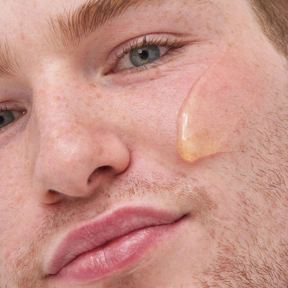 Close-up of a young man applying The INKEY List C50 Serum on his cheek for clear and revitalized skin.