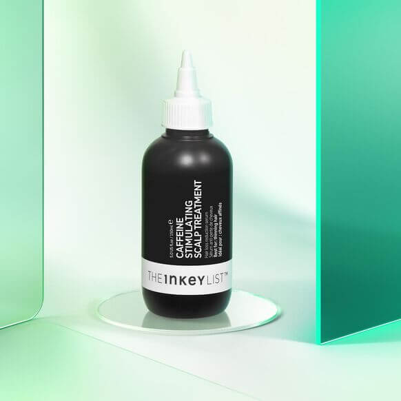 The INKEY List Caffeine Stimulating Scalp Treatment bottle on a reflective surface with a modern background.