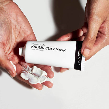 Hands holding a tube of The Inkey List Kaolin Clay Mask with visible product on fingers against a white background