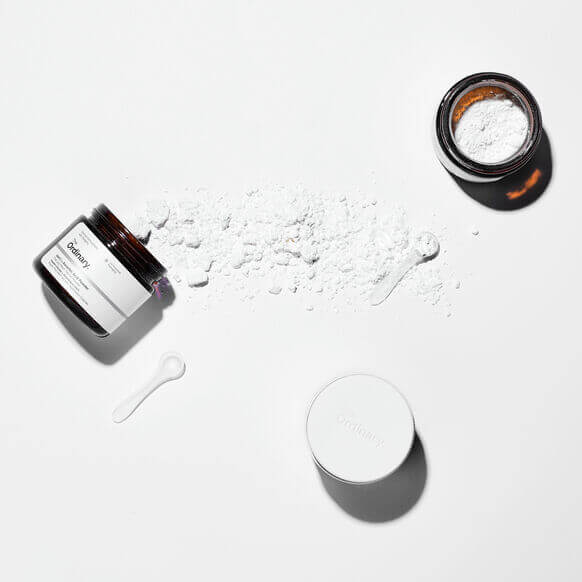 The Ordinary 100% L-Ascorbic Acid Powder, vitamin C in a jar, with powder spilled and measuring spoon.