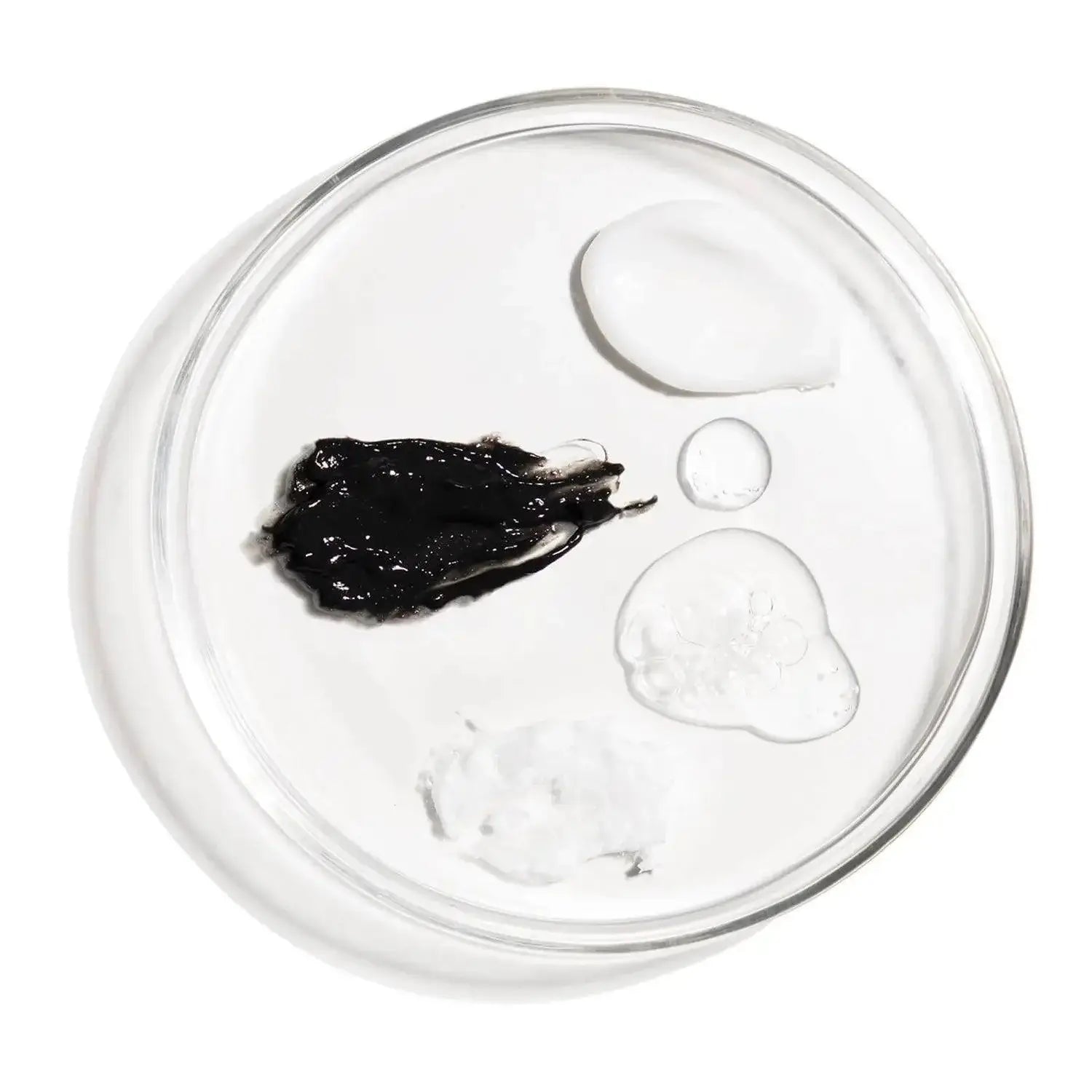 Close-up of various skincare products' textures including black, clear, and white creams on a glass dish.