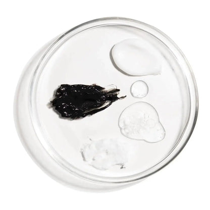 Close-up of various skincare products' textures including black, clear, and white creams on a glass dish.