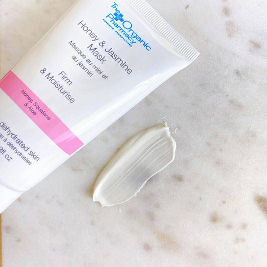 The Organic Pharmacy Honey & Jasmine Mask with cream on marble surface, revitalizes and moisturizes skin.