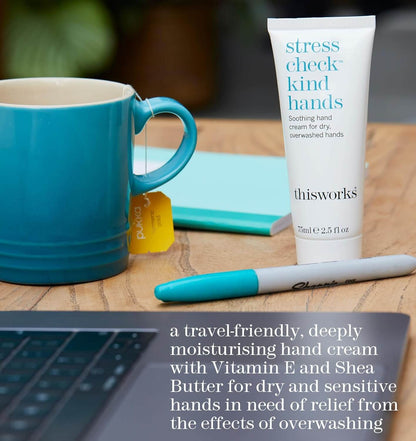 thisworks Hand cream tube labeled 'stress check kind hands' next to a blue mug and pen on a wooden surface.