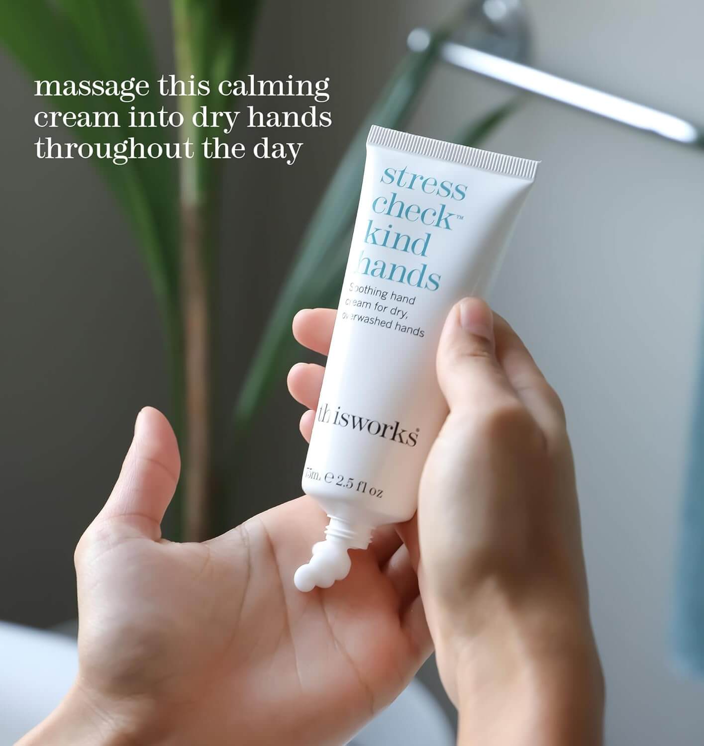 Hand holding a tube of 'thisworks stress check kind hands' cream with text on a blurred background