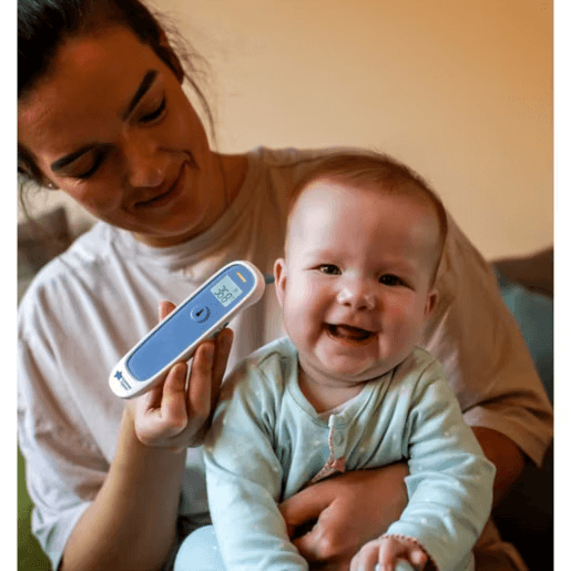 Woman holding a baby and a digital thermometer with a QR code, smiling.