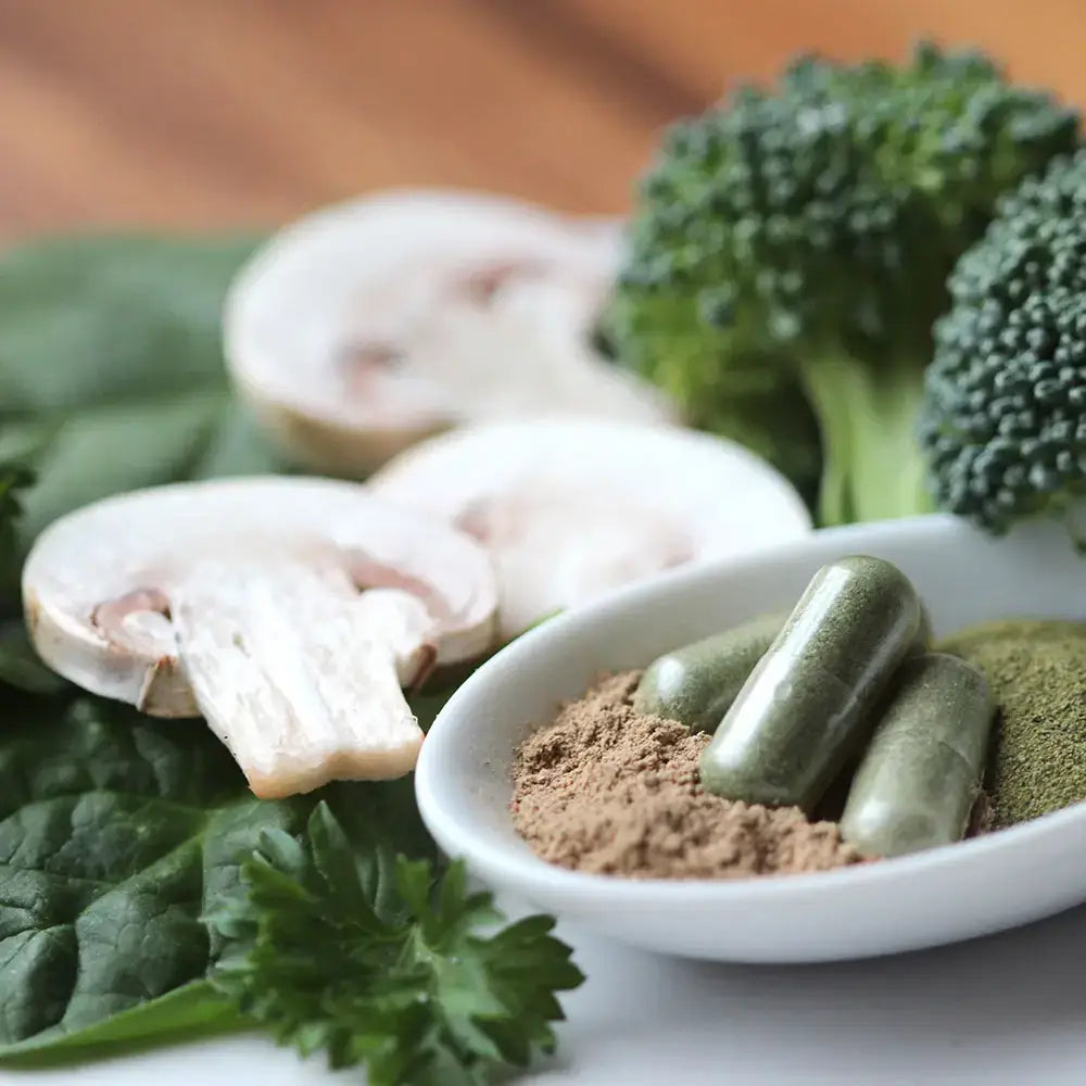 Fresh superfoods like mushrooms, spinach, and broccoli beside Touchstone Essentials Supergreens +D capsules.
