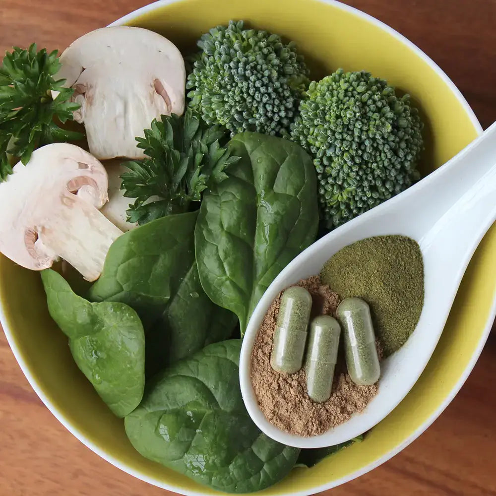 Bowl of fresh superfoods with spinach, broccoli, mushrooms, and green capsules for Touchstone Essentials supplement.