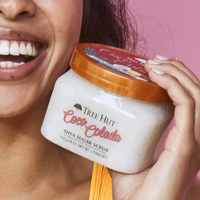 Person holding a jar of Tree Hut Coco Colada Shea Sugar Scrub against a pink background