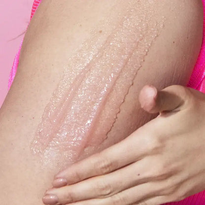 Close-up of a hand applying TREE HUT Cotton Candy Shea Sugar Scrub a pinkish-rose lotion or cream to a shoulder.