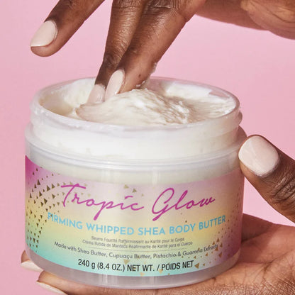 Jar of Tree Hut Tropic Glow Whipped Shea Body Butter with hand scooping out cream against a pink background