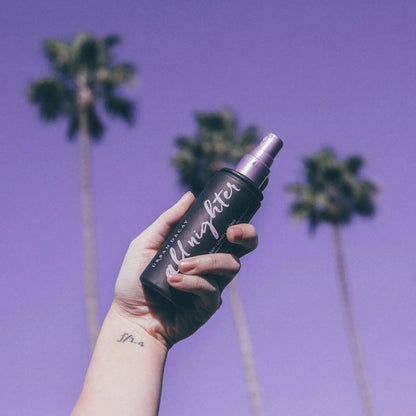 Urban Decay All Nighter Setting Spray held in hand against a purple sky with palm trees, perfect for long-lasting makeup.