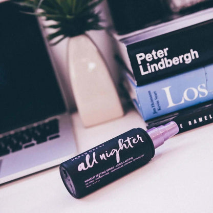 Urban Decay All Nighter Setting Spray bottle on a desk with books, showcasing its long-lasting makeup hold.