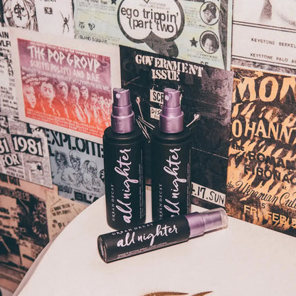 Urban Decay All Nighter Setting Spray trio against a vintage poster backdrop, perfect for long-lasting makeup.