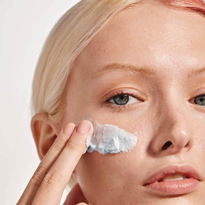 Model applying VERSED Keep The Peace Blemish-Calming Cream Cleanser on her face to soothe acne-prone skin.