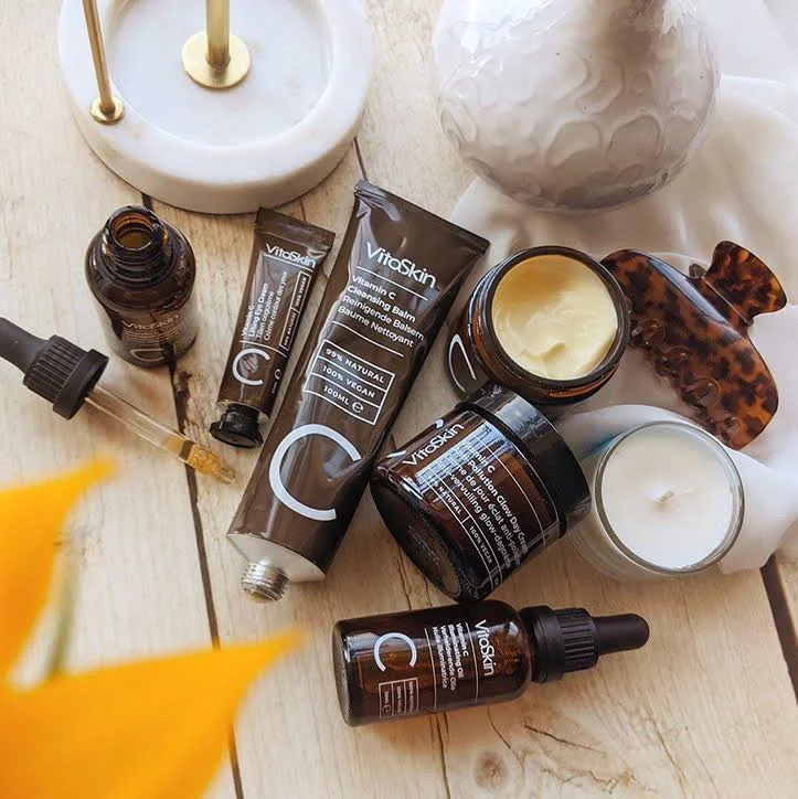Vitaskin skincare products arranged on a wooden surface with a flower, showcasing Vitamin C Cleansing Balm and serums.