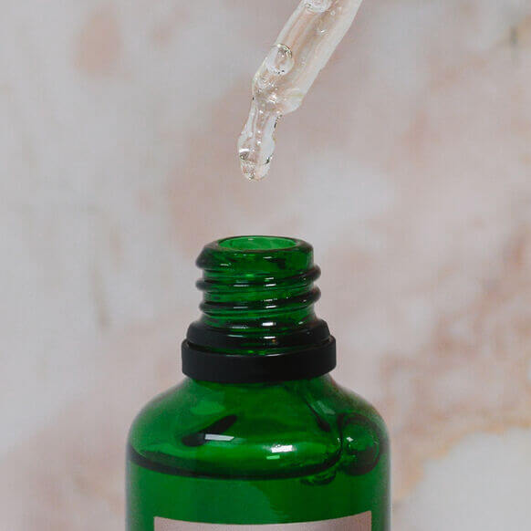 Votary Brightening Hyaluronic Serum bottle with dropper releasing serum, promoting radiant skin and hydration.