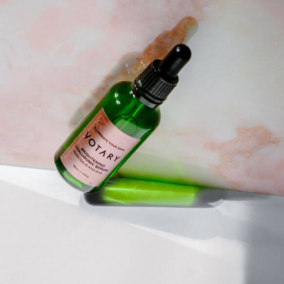 Votary Brightening Hyaluronic Serum 50ml on a light background with a pipette, showcasing its vibrant green bottle.