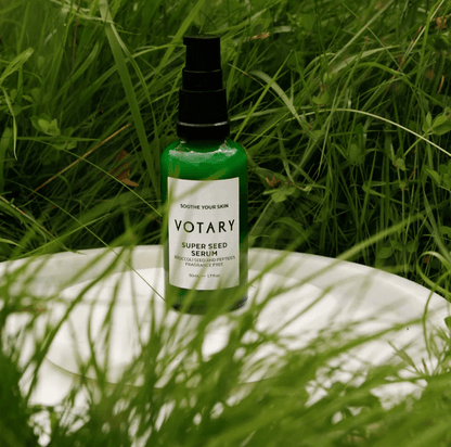 Votary Super Seed Serum bottle surrounded by lush green grass on a white plate.