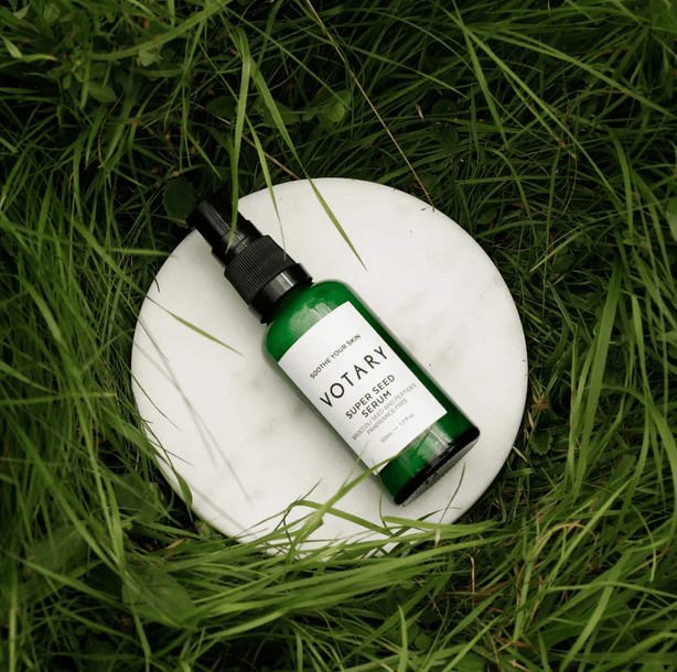 Votary Super Seed Serum in green bottle on a marble surface, surrounded by grass, showcasing natural skincare.