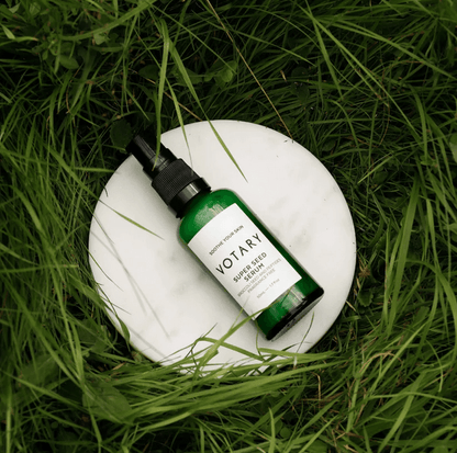 Votary Super Seed Serum in green bottle on a marble surface, surrounded by grass, showcasing natural skincare.