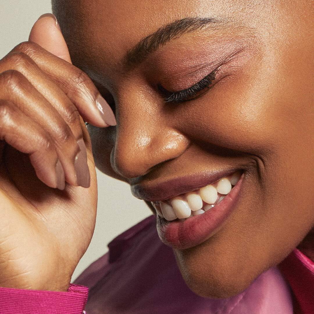 Close-up of a woman with a soft smile, wearing a pink top. e.l.f.