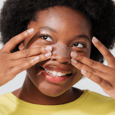 Woman applying ZITSTICKA GOO GETTER™ Nose strip on her nose to remove blackheads and whiteheads.