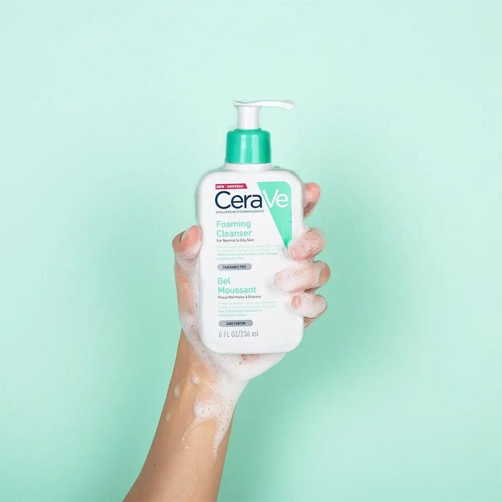 Person holding CeraVe Foaming Cleanser with bubbly foam on a mint green background, ideal for normal to oily skin.