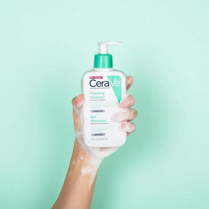 Person holding CeraVe Foaming Cleanser with bubbly foam on a mint green background, ideal for normal to oily skin.