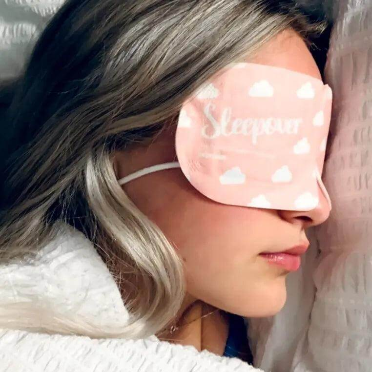 Woman wearing Popmask Sleepover self-warming steam eye mask with cloud design, promoting relaxation and sleep.