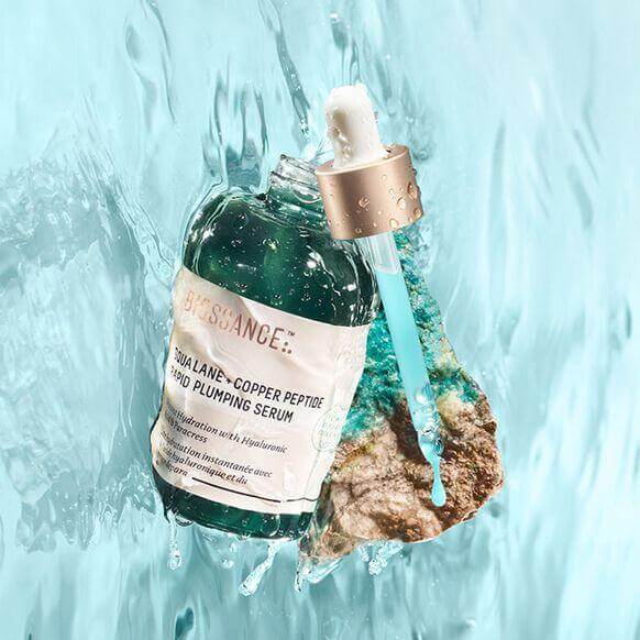 Biossance Squalane and Copper Peptide Rapid Plumping Serum 50ml with a dropper, surrounded by water for hydration effect.