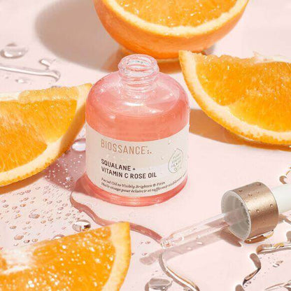 Biossance Squalane + Vitamin C Rose Oil with fresh oranges on a pink background, highlighting hydration and glow.