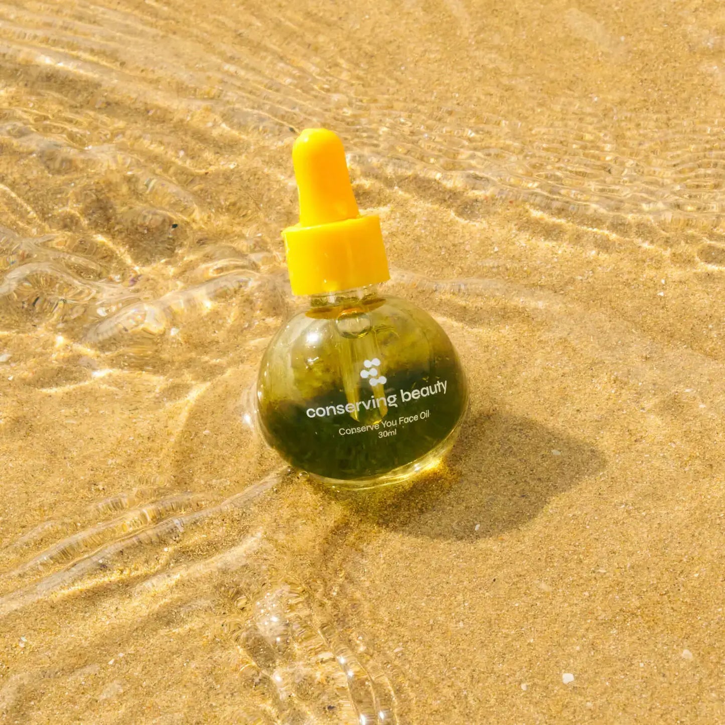 Conserving Beauty Conserve You Face Oil bottle on sand, showcasing its plant-based formula for a radiant complexion.