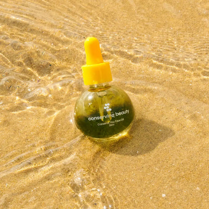 Conserving Beauty Conserve You Face Oil bottle on sand, showcasing its plant-based formula for a radiant complexion.
