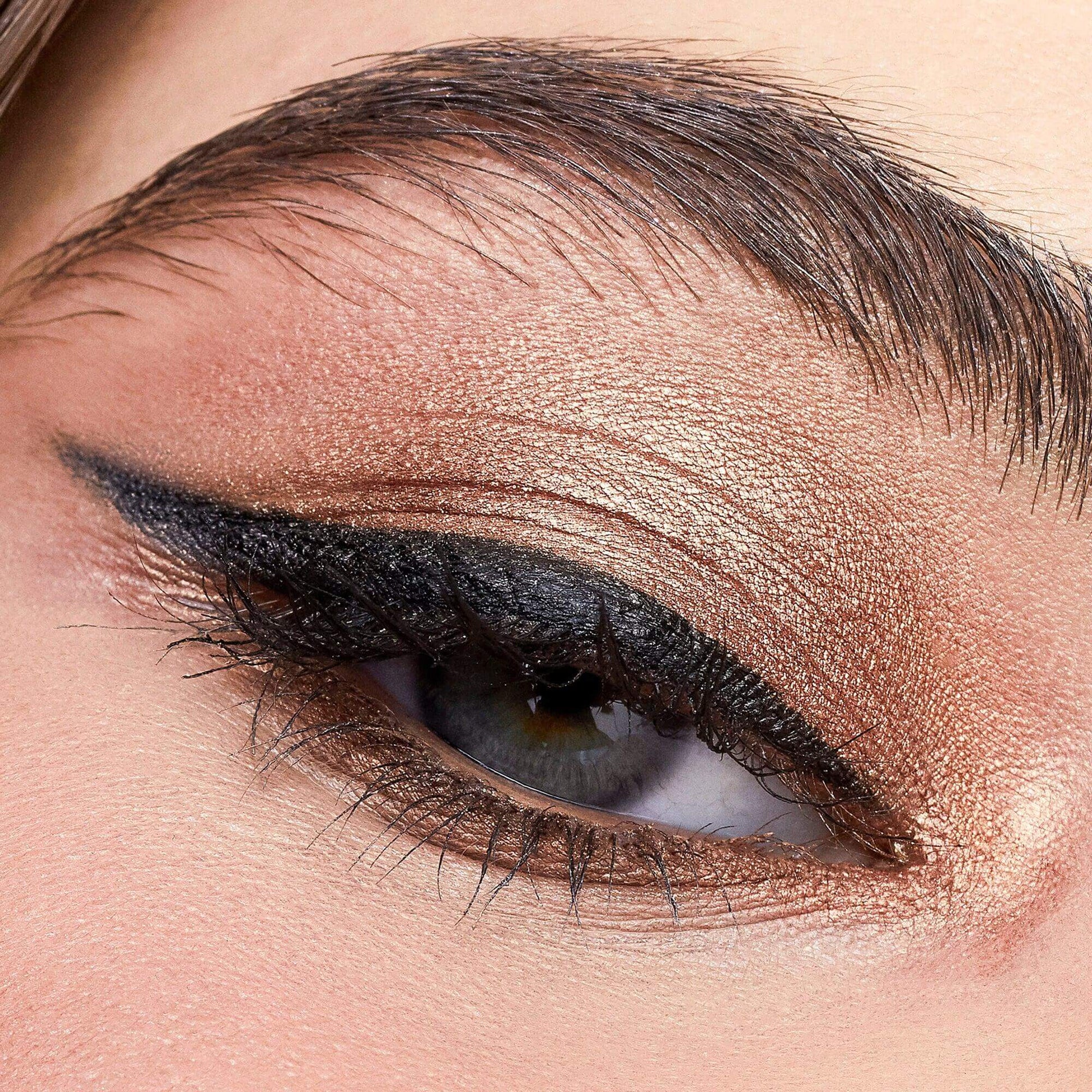 Close-up of an eye showcasing shimmery bronze eyeshadow with bold eyeliner, exemplifying e.l.f. Bite Size Eyeshadow in Pumpkin Pie.