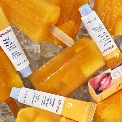 Glossier Balm Dotcom Mango lip balm tubes and mango popsicles on ice, showcasing hydration and vibrant color.
