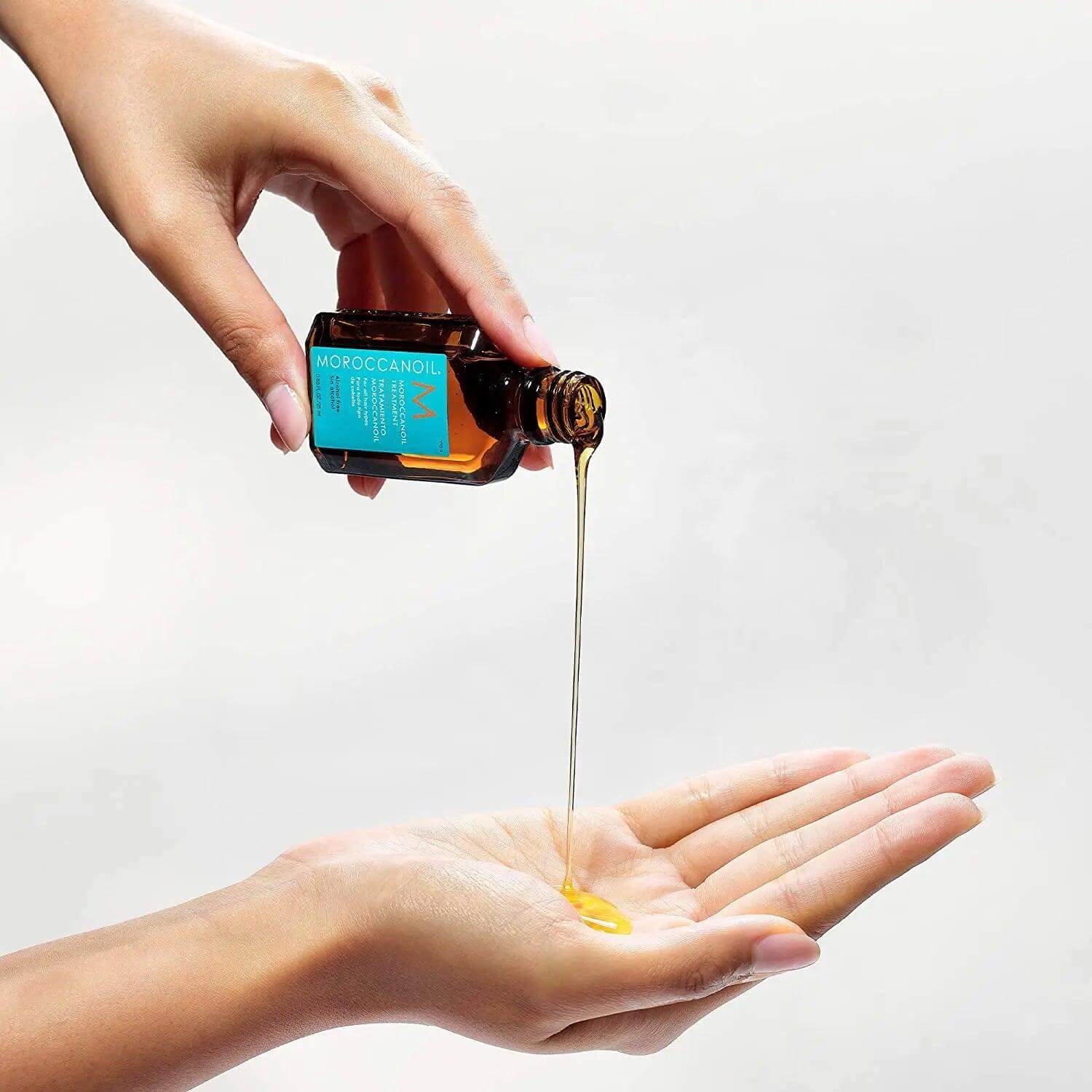 Person pouring Moroccanoil Treatment 25ml into palm, showcasing its lightweight, silky hair product.