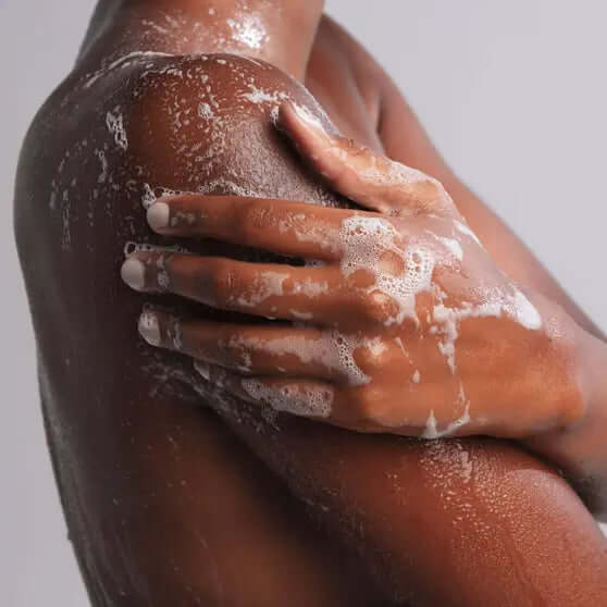 Close-up of a person washing their shoulder with OUAI creamy lather, showcasing hydration and cleansing benefits.