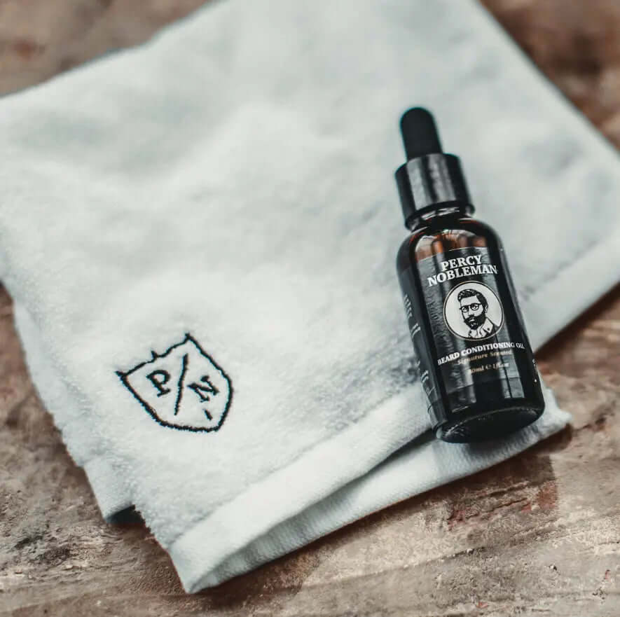 Percy Nobleman Signature Beard Oil 30ml bottle next to a soft towel featuring logo, perfect for beard care routines.